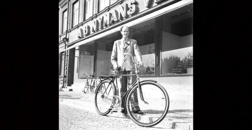 Man bredvid cykel framför en byggnad där skylten Nymans verkstäder skymtar i bakgrunden.